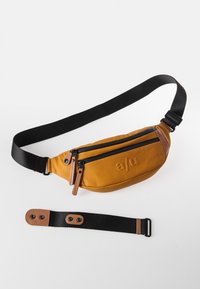 Bruine leren heuptas met zwarte ritsen, verstelbare zwarte schouderband, geperst logo en contrasterende tan accenten. Glad textuur, ovale vorm.