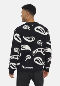 Fluffy gebreide trui met een donkerblauwe basis en witte abstracte patronen, met een ronde hals en lange mouwen.