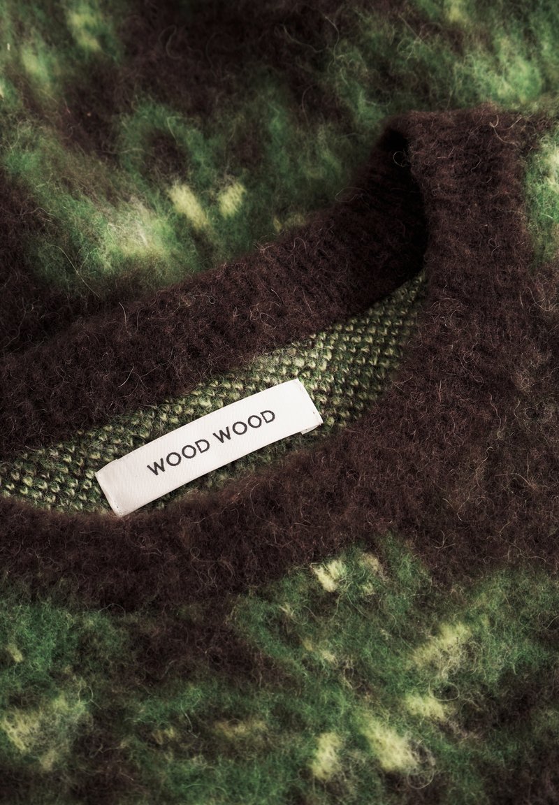 Pull en laine à motifs verts et marron avec un col texturé et une étiquette blanche portant la mention "WOOD WOOD" cousue à l'intérieur du cou.