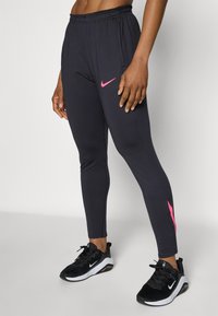 Sorte svarte treningstights med elastisk midje. Har en rosa Nike swoosh-logo på venstre lår og en innsnevret passform. Teksturert stoff.