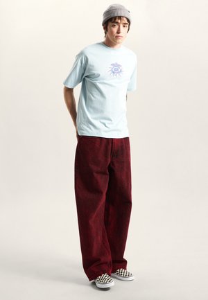 Light blue cotton t-shirt with a purple graphic, paired with red patterned wide-leg jeans and black and white checkered slip-on shoes.