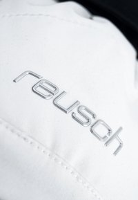 Tissu blanc avec une texture lisse, arborant un logo métallique argenté "reusch" bien en évidence. Couture visible le long du bord.