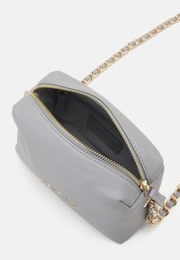 Borsa a tracolla in pelle grigia con finitura texturizzata, cerniera color oro e tracolla a catena. L'interno presenta una tasca con cerniera e un'etichetta del marchio.