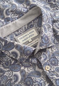 Camicia con motivo a paisley grigio chiaro e blu. Presenta un colletto con bottoni e un'etichetta con la scritta "COLOURS & SONS," taglia L. Tessuto morbido.