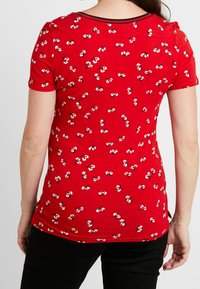 Röd kortärmad skjorta i mjukt material, med ett sprängt mönster av vita blommor och en kontrasterande svart krage.