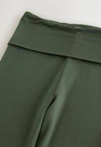Dunkelgrüne Leggings mit einem breiten, gefalteten Taillenbund, aus weichem, dehnbarem Material mit glatter Textur.