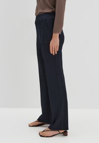 Navyblauwe, wijde broek van zacht stof, met een hoge tailleband en twee zijzakken, gecombineerd met zwarte bandjesandalen.