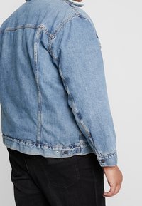 Ljusblå denimjacka med klassisk design, som har knäppning framtill, sidfickor och sydda sömmar. Texturerat tyg synligt.