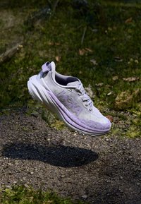 Scarpa da running HOKA di un leggero viola, con tessuto texture, suola curva e sistema di allacciatura, che presenta un logo prominente sul lato.
