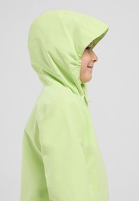 Giacca impermeabile verde chiaro con cappuccio, dalla texture liscia, elastico sul cappuccio e chiusura con zip frontale completa, indossata da un bambino.