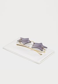 Lilla tähtkujuline päikseprillide paar kuldse metalsangaga, mis puhkab valgel karbil. Omab toonitud objektiive ja minimalistlikku disaini.