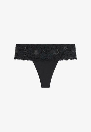 Černé tangá krajkového stylu s širokým květinovým pasem a zvlněnými okraji, vystavené na bílé ploše.