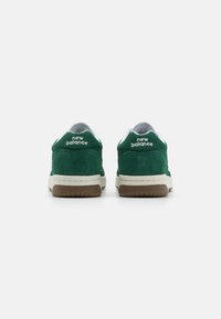 Green suede sneakers with white accents, featuring a cushioned collar, thick rubber sole, and embroidered logo on the back.