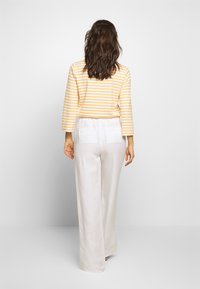 Yellow and white striped long-sleeve top paired with loose-fitting white pants; both made from light, textured fabric.
