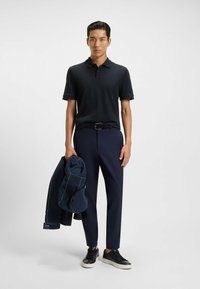 Marinblå pikétröja med korta ärmar, matchad med marinblå tapered-byxor, ett svart bälte och svarta sneakers. En marinblå jacka hänger över armen.