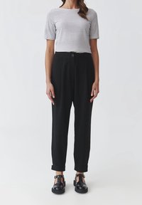 Pantalones negros de cintura alta con un corte relajado, combinados con una blusa de manga corta a rayas blancas y negras. Calzado negro con detalle de hebilla.