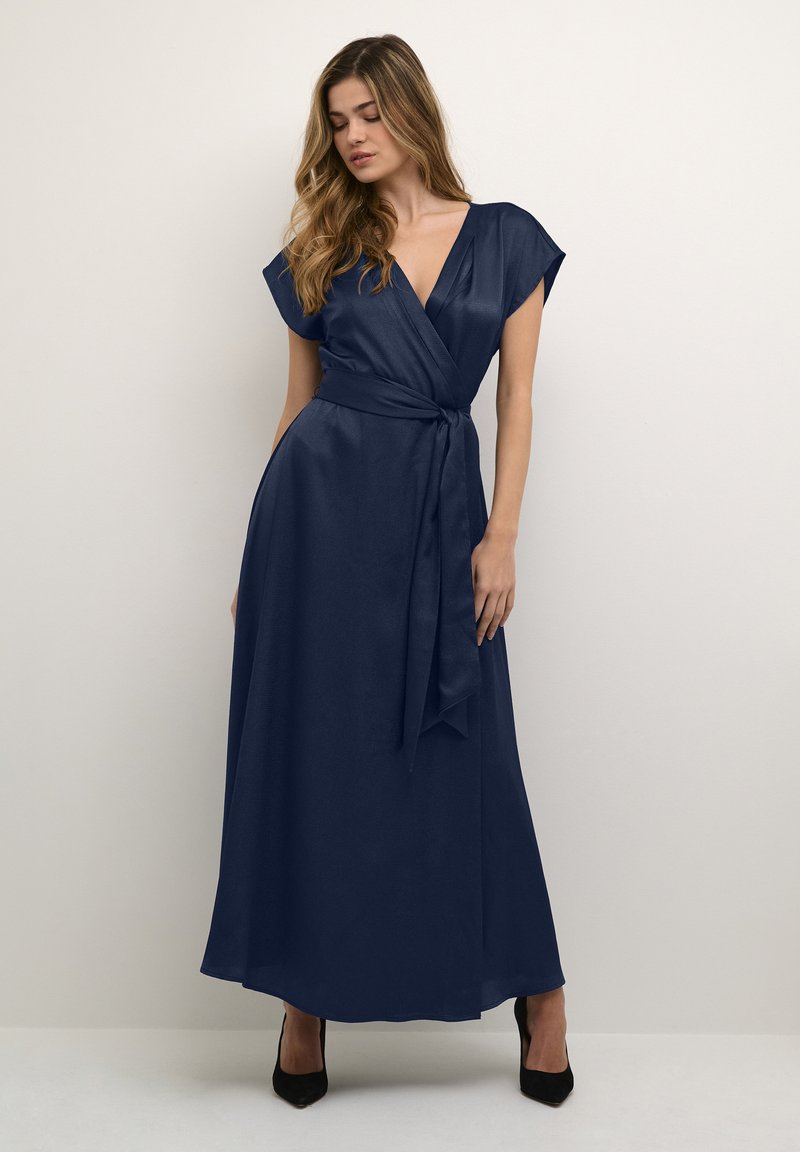 Marineblaues Wickelkleid mit kurzen Ärmeln, strukturiertem Stoff und einem Bund in der Taille, bodenlang, kombiniert mit schwarzen High Heels.