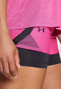 Pantaloni sportivi rosa con accenti neri, realizzati in poliestere liscio, dotati di un pannello in rete per la ventilazione e un logo stampato sul lato.