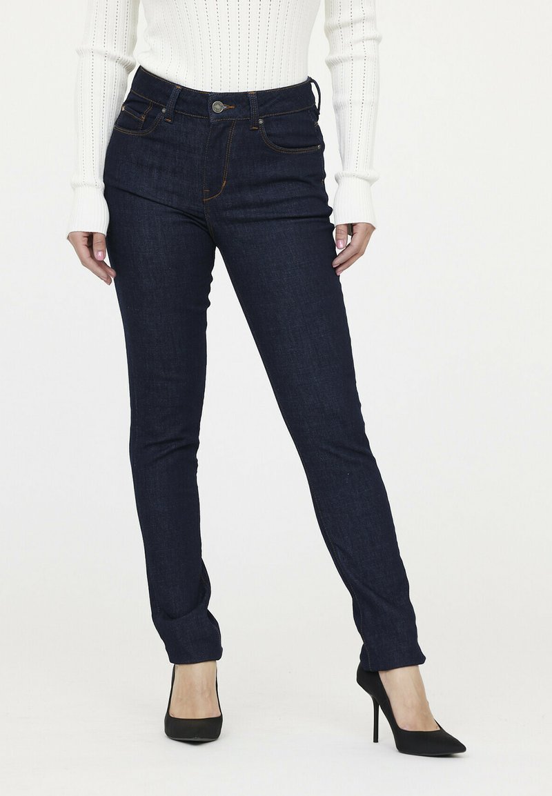 Dunkelblaue Denim-Jeans im Slim-Fit mit einem Fünf-Taschen-Design und kontrastierender Naht. Kombiniert mit einem weißen gerippten Langärmeloberteil.