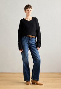Black, fluffy sweater with wide sleeves, paired with high-waisted blue jeans and brown leather ankle boots. Simple belt detail. Neutral background.