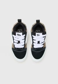 Des baskets Vans en noir et blanc avec des lacets blancs et des détails en imprimé léopard sur les côtés et le talon, vues d'en haut sur un fond blanc.