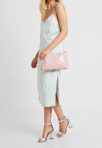 Světle modré saténové šaty na ramínka s postranními rozparky, doplněné o růžovou texturovanou kabelku a stříbrné sandály na blokovém podpatku se zapínáním.