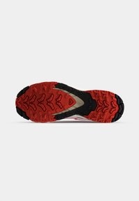 Suola di scarpe da trail running con un pattern di trazione in gomma nera robusta, con accenti rossi e un profilo per una migliore aderenza e stabilità.
