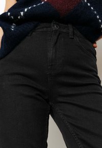 Jeans en denim noir au design ajusté, dotés de détails de couture discrets, de poches avant et d'une fermeture à bouton classique à la taille.