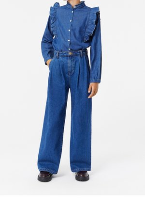 Person wearing high-waisted wide-leg blue jeans and a blue denim long-sleeve blouse with ruffled shoulders and button closure.