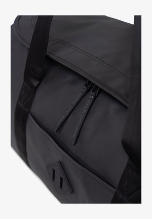 Sac de sport noir avec une texture lisse, doté de doubles fermetures éclair et d'un design en tissu durable. Comprend un accent avec logo et des sangles plates.