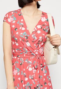 Robe portefeuille à motif floral en corail avec des manches courtes, présentant une taille ceinturée, des motifs vibrants en rose, blanc et bleu canard. Texture de tissu lisse.