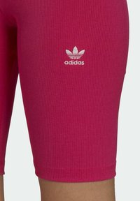Różowe, prążkowane spodenki kolarskie o dopasowanym kroju, z małym białym logo Adidas po lewej stronie. Gładka faktura; długość do kolan.