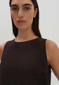 Top senza maniche marrone con tessuto testurizzato, scollatura rotonda e design minimalista, che mette in risalto la zona delle spalle e della clavicola.