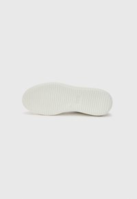 Semelle de sneaker blanche, plate avec une texture lisse. Présente des rayures horizontales pour l'adhérence. Bout arrondi et design de talon semi-circulaire.