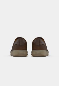 Zapatos de piel marrón con forma redondeada y perfil bajo, que presentan una superficie texturizada y suelas de goma beige con una marca sutil.