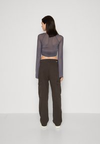Haut gris à manches longues, ajusté, semi-transparent avec un dos froncé ; associé à un pantalon cargo marron foncé avec des poches latérales. Chaussures blanches unies.