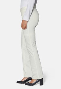 Weiße Jeans mit einem Schlagdesign, hohen Bund, zwei Gesäßtaschen und dezenten Nähten. Kombiniert mit schwarzen High Heels.