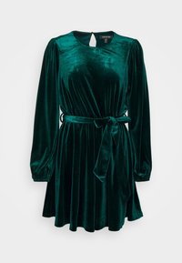 Grön sammetklänning med långa puffärmar, en cinchad midja och en rosettdetalj vid midjan. Har en rund halsringning och en nyckelhålsback.