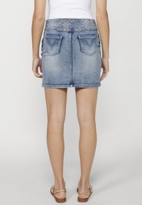 Jupe en denim avec un délavage bleu clair, dotée d'une taille brodée texturée, de poches arrière et d'un design droit et ajusté.