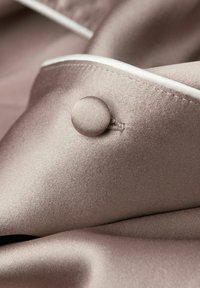 Knäppt blus i mjuk mauve-satin, med en rund tygknapp och vit piping längs kragen. Slät textur med subtil glans.