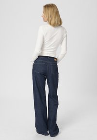 Mörkblå denimbyxor med vida ben har en bakfickdesign och en läderetikett på midjan. Tillsammans med en åtsittande vit ribbad topp.