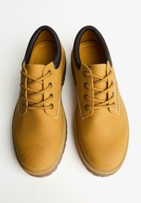 Pantofi din suede galben, cu vârf rotund, accente din piele marron și un design cu șase găuri pentru șireturi. Suprafață texturată cu talpă din cauciuc.