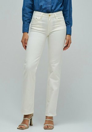 Femme portant un jean blanc taille haute à coupe droite, associé à des sandales à talons beiges et une chemise en jean bleue à manches longues.