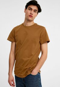 Brun bomulds t-shirt med rund halsudskæring og korte ærmer, der har en afslappet pasform og glat tekstur, parret med blå denimjeans.