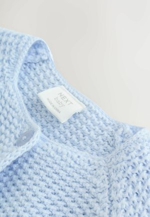 Lyseblå strikket baby cardigan med knap og "Next baby" label indeni kraven, vist på hvid baggrund.