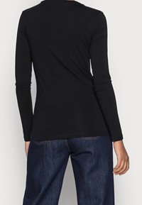 Zwarte longsleeve met ronde halslijn, gemaakt van zachte rekbare stof en een slanke pasvorm, gecombineerd met donkerblauwe jeans. Eenvoudig ontwerp.