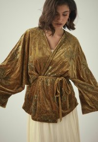 Velour kimono i olivengrøn med indviklet guld blomsterbroderi og perler, med brede ærmer og en bindebånd i taljen.