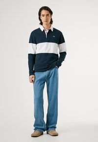 Marineblå og hvide stribede langærmede polo med krave, parret med lyseblå jeans og beige slip-on sko. Enkelt logo på skjorten.