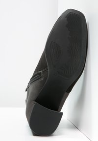 Schwarze Wildleder-Stiefelette mit einer strukturierten Gummisohle. Mit einem seitlichen Reißverschluss und der Größe 37 auf der Sohle gekennzeichnet.