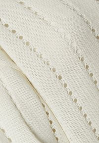 White knitted fabric features a textured pattern with evenly spaced circular cutouts, creating a delicate and airy appearance.